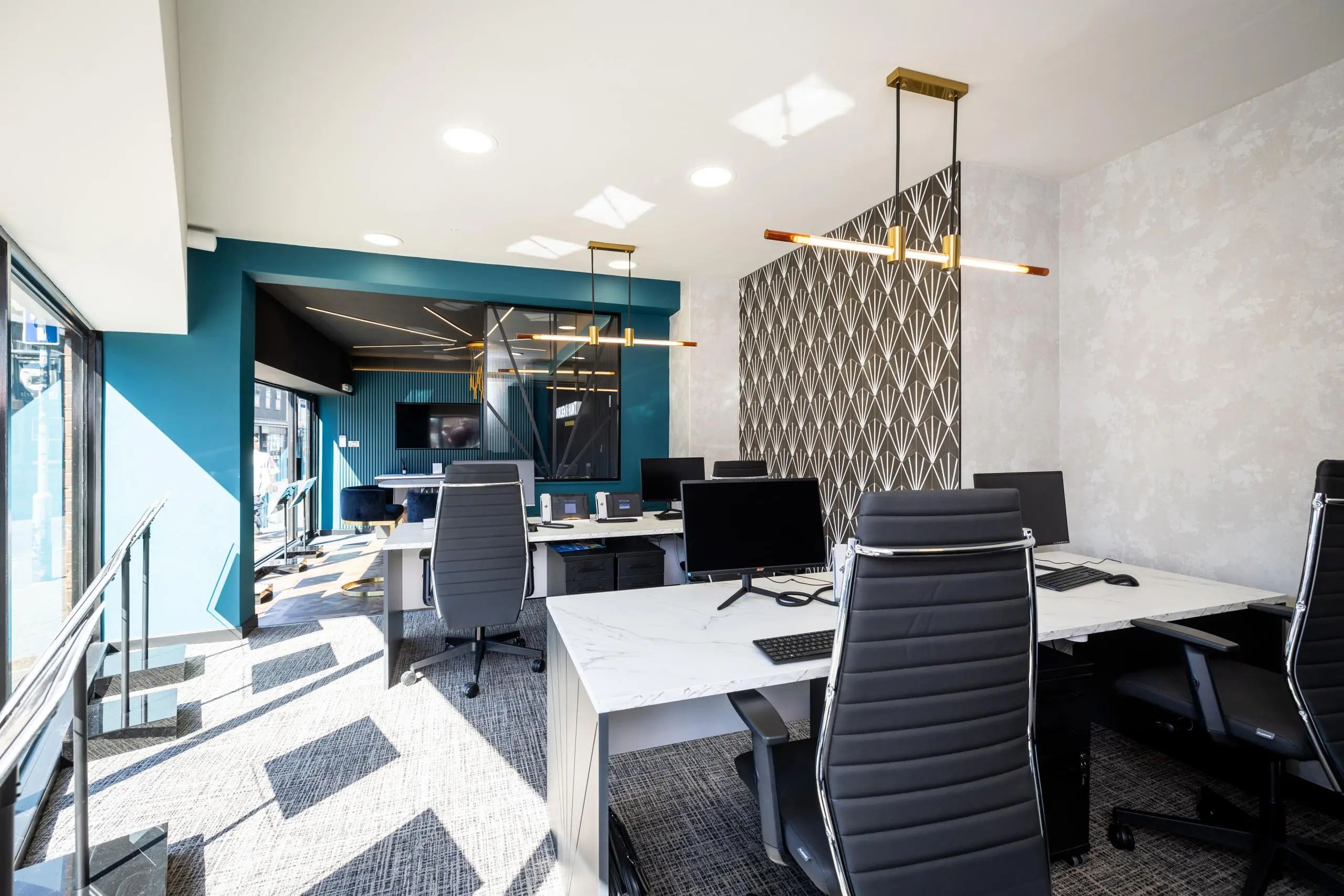 Modern office space with white desks, black office chairs, computer monitors, teal accent wall, patterned screen divider, and geometric floor design
