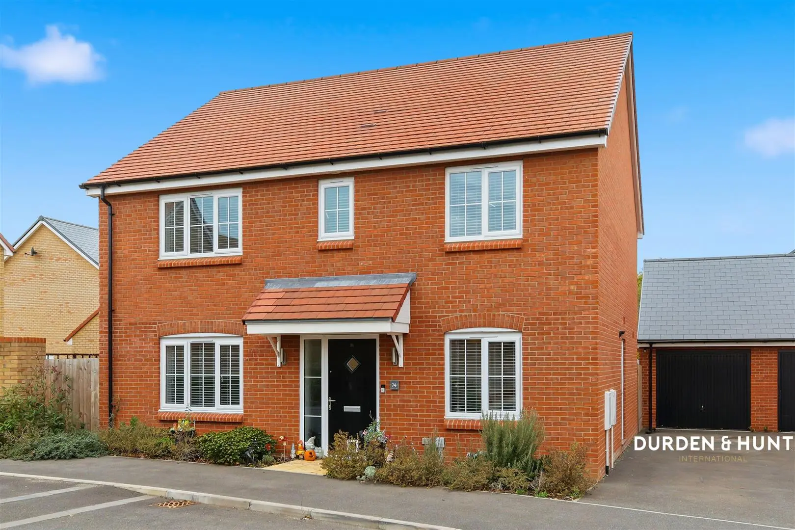 Red brick detached house with terracotta tiled roof, white-framed windows, and covered entrance porch