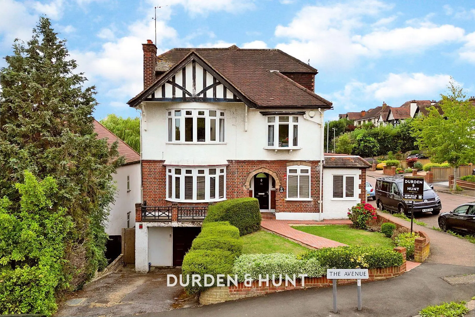 Two-storey brick and white rendered house with Tudor-style gable, bay windows, and tiled roof. "The Avenue" street sign visible. Durden & Hunt estate agent sign on driveway.