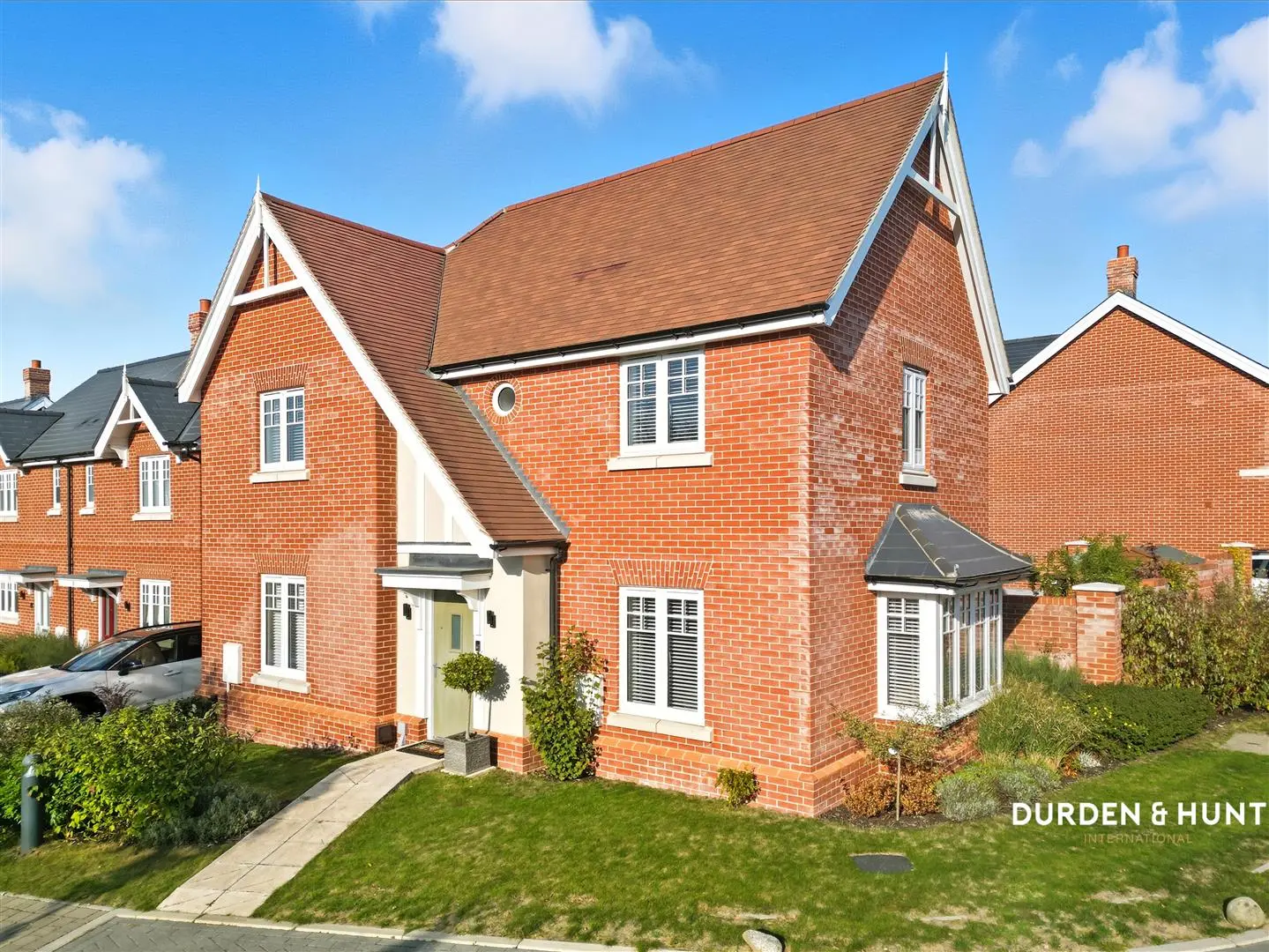 Modern red brick detached house with pitched roof, white-framed windows, cream entrance door, and front garden