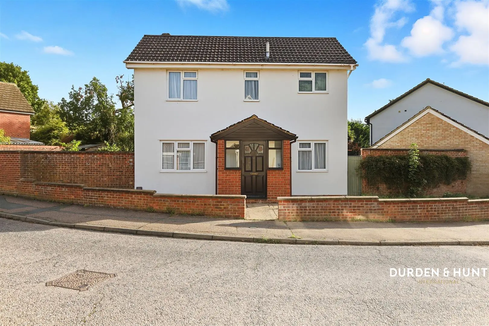 Two-storey detached house with white render and dark tiled roof, red brick porch, brick boundary walls, and driveway