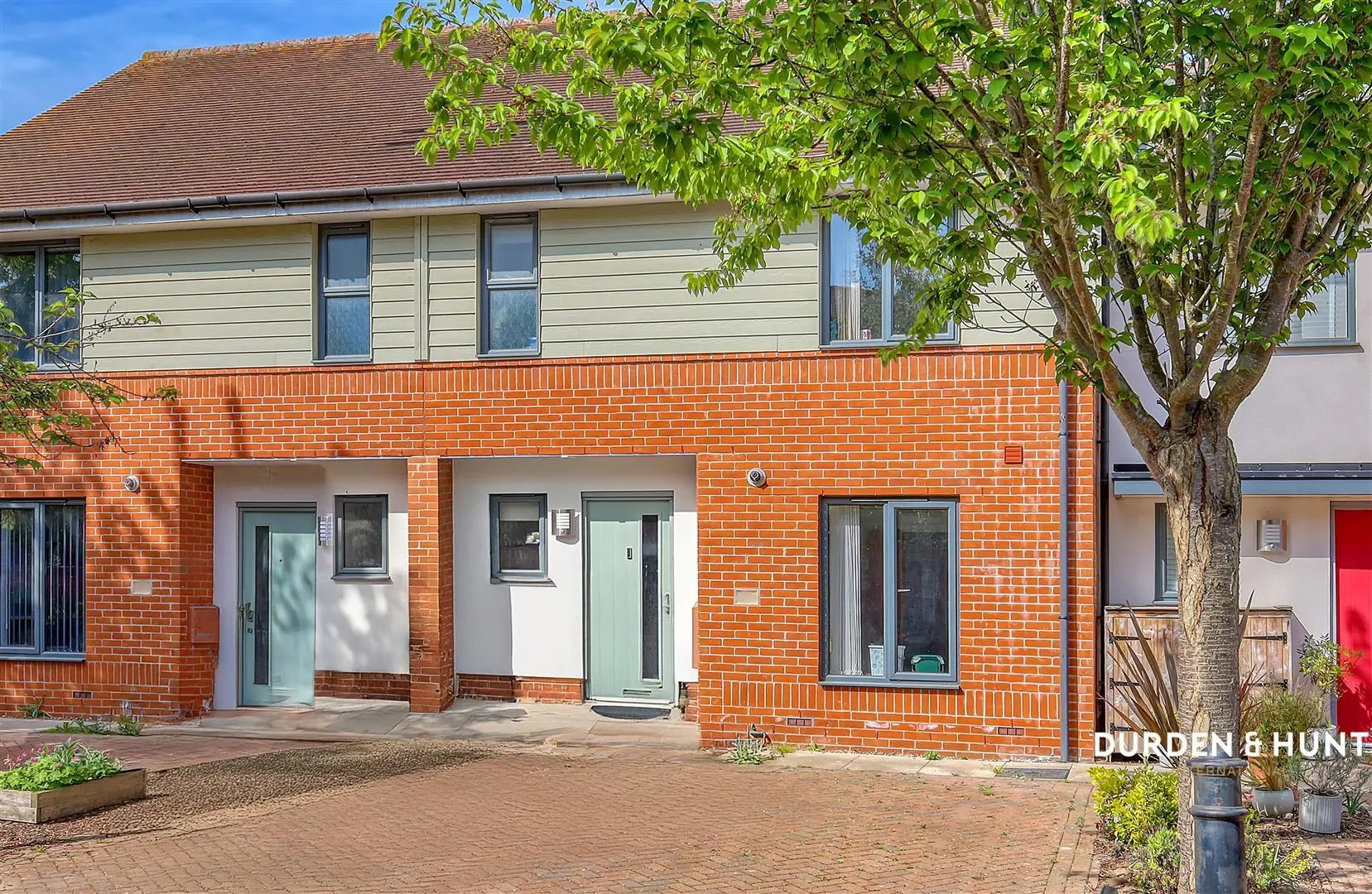 Modern brick townhouse with cream-coloured upper storey, three entrance doors, and mature tree in front garden