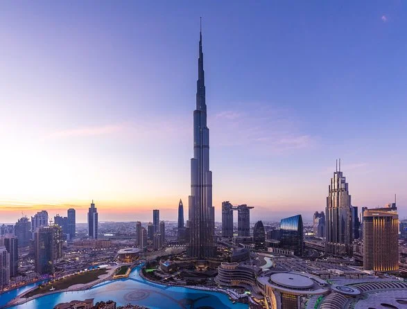 Aerial view of a city skyline at dusk with a prominent tall tower in the centre, surrounded by modern buildings and a curved waterway