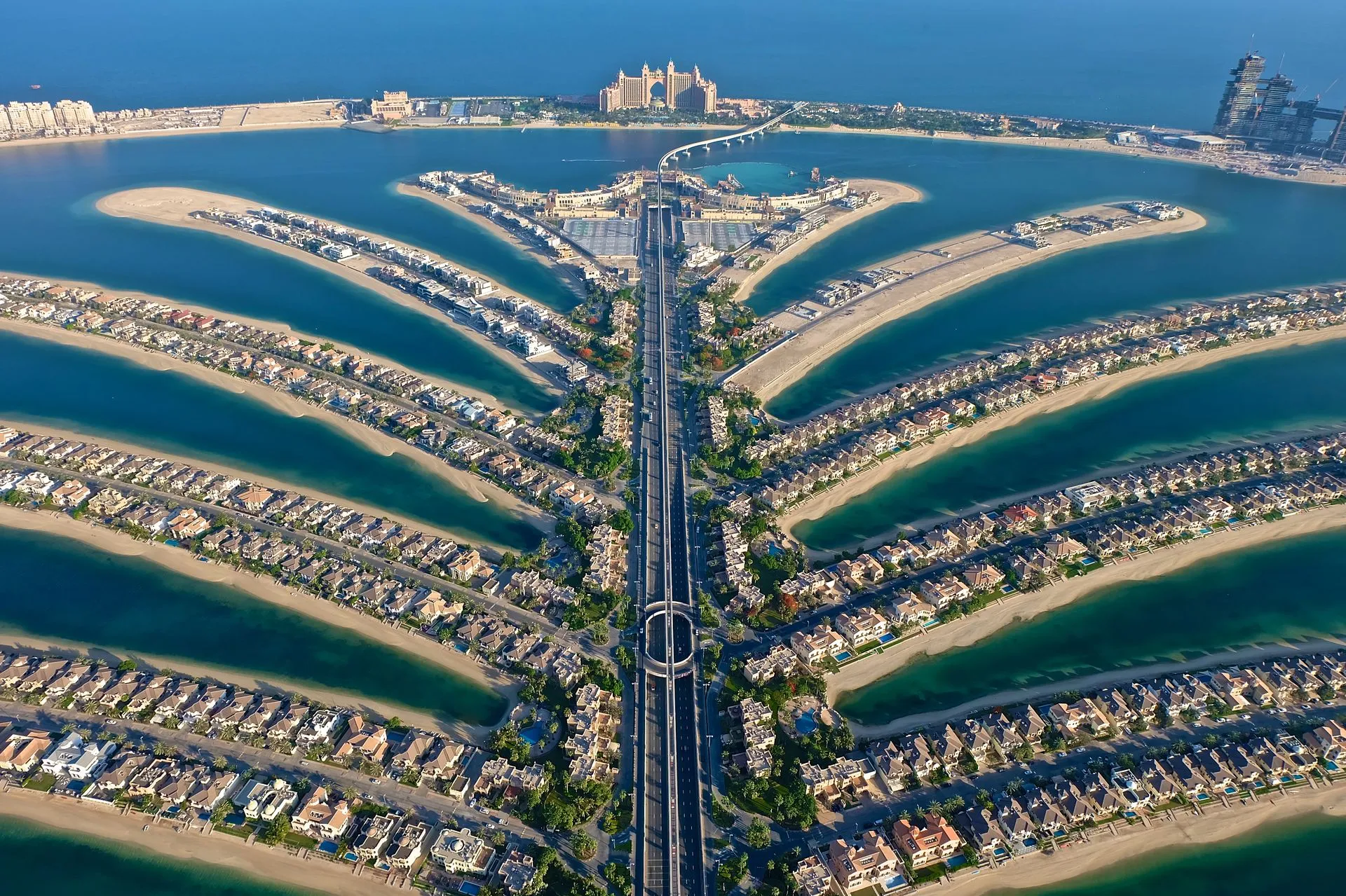 Aerial view of Palm Jumeirah, Dubai, showing palm-shaped islands with residential villas, waterways, and central boulevard, with Atlantis hotel and coastline in background