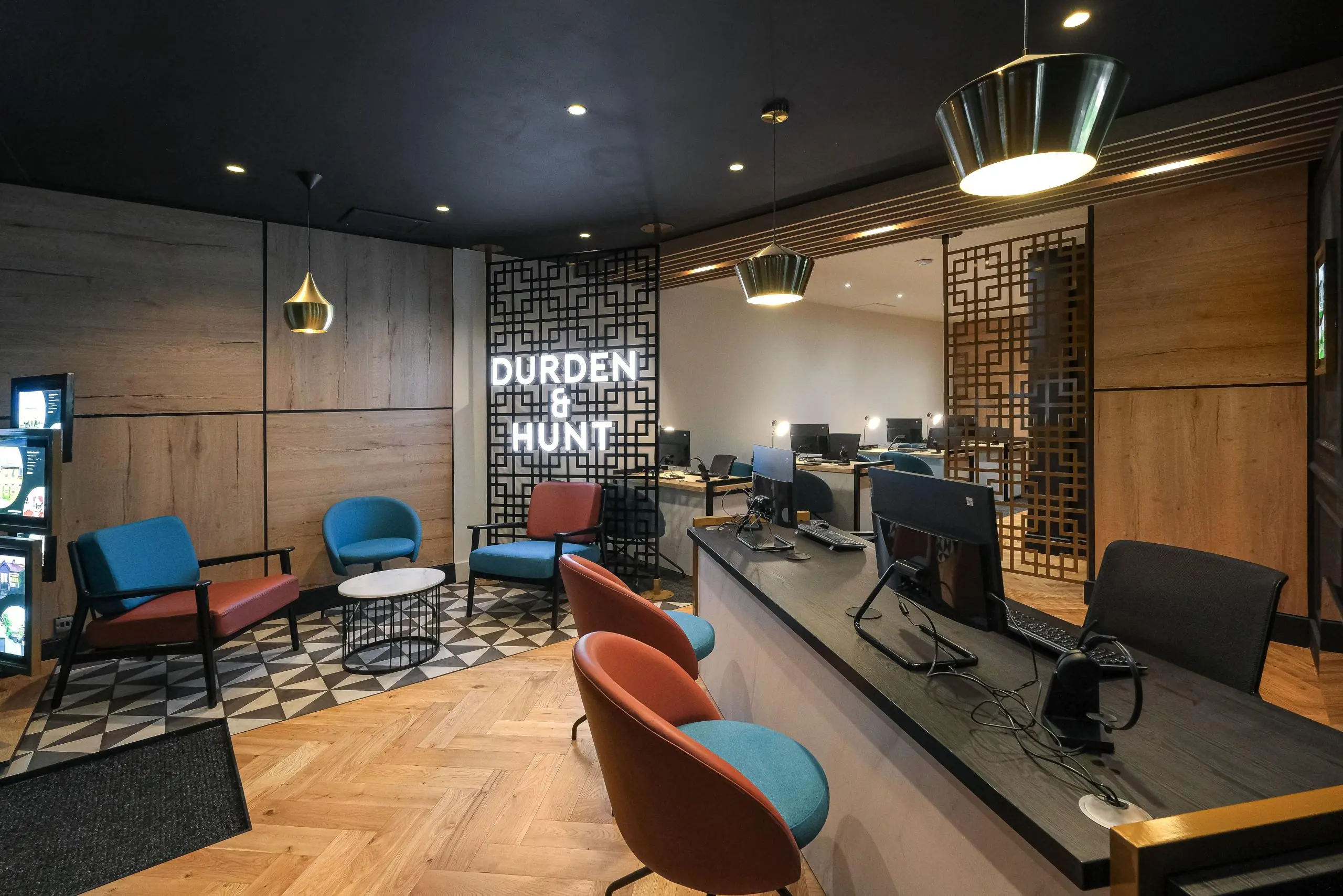 Modern office interior with reception area, blue and orange chairs, wooden panelling, geometric screens, and "Durden & Hunt" signage on wall