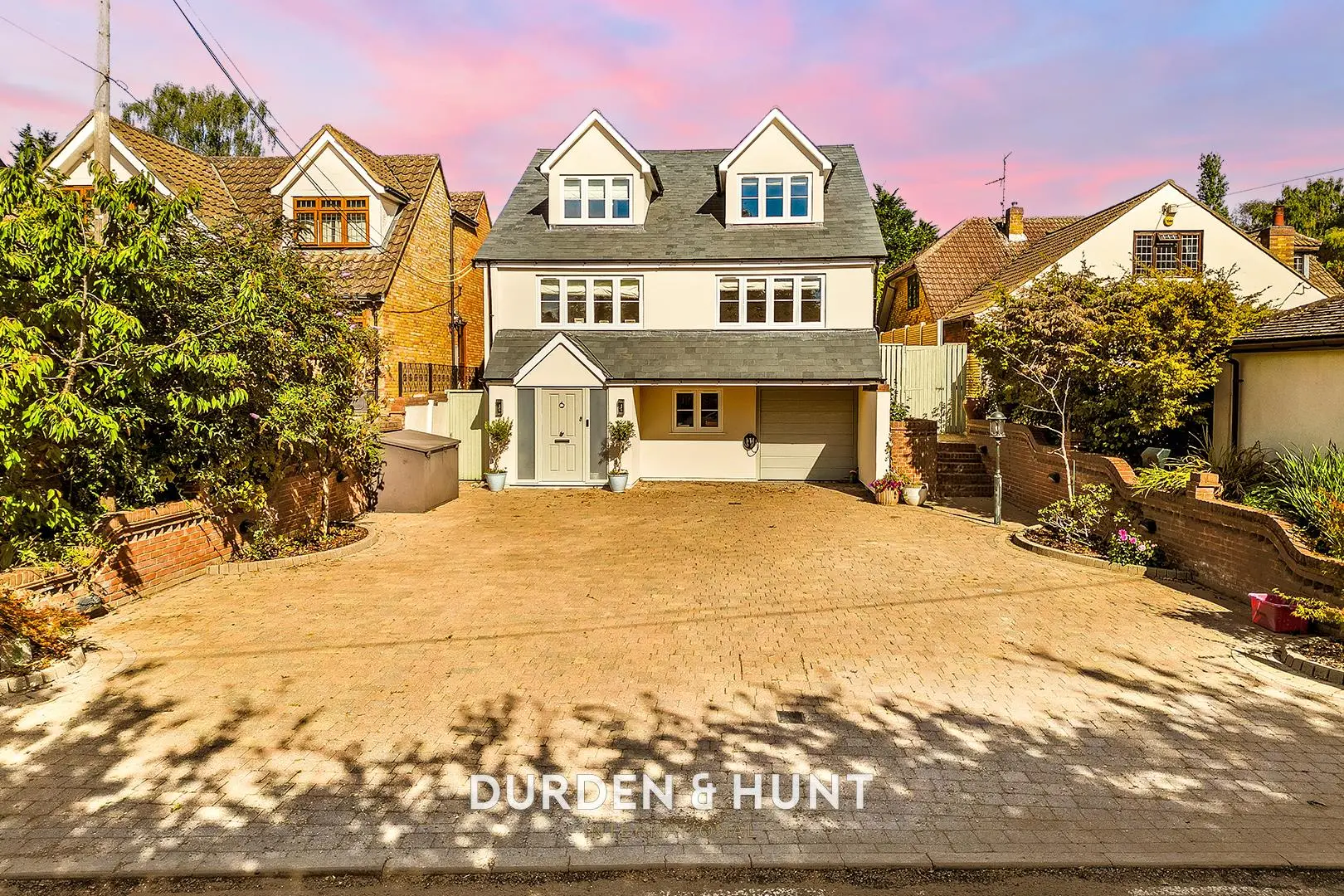 Modern two-storey detached house with cream and grey exterior, double garage, dormer windows, and paved driveway. Durden & Hunt branding visible.