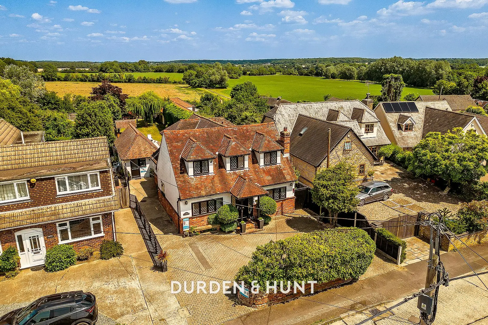 Aerial view of residential properties with red-tiled roofs, brick and rendered walls, surrounded by green fields and trees, with "DURDEN & HUNT" text overlay