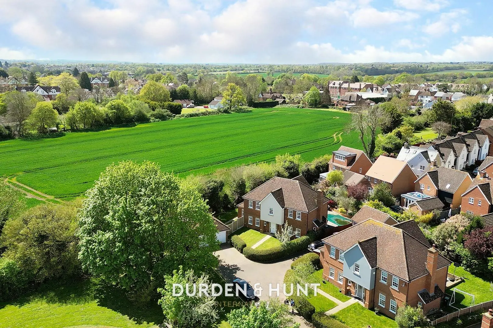 Aerial view of residential properties and green fields in a village setting, with "DURDEN & HUNT INTERNATIONAL" text overlay