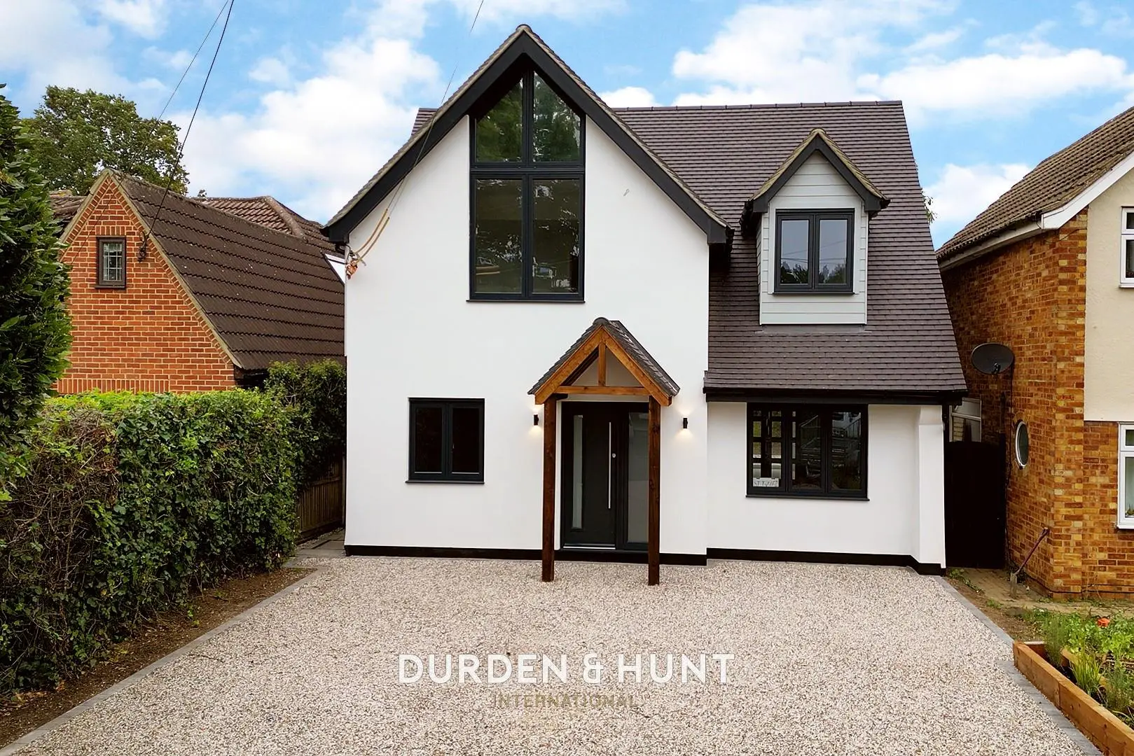 White and grey rendered house with black windows and wooden porch, gravel driveway, brick neighbours either side