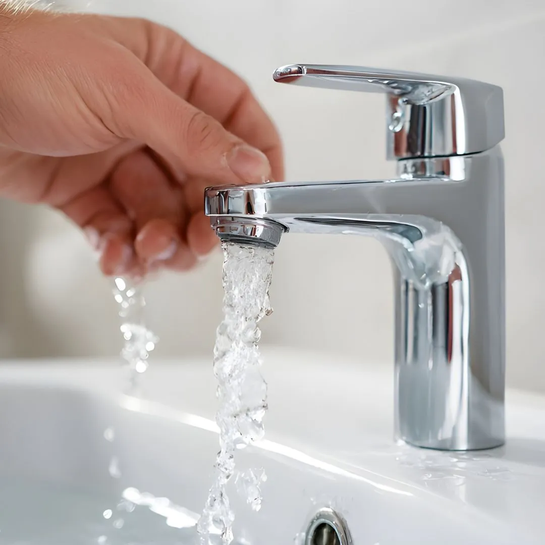 Hand turning on a modern tap with running water in a bathroom sink, showing working plumbing and water supply