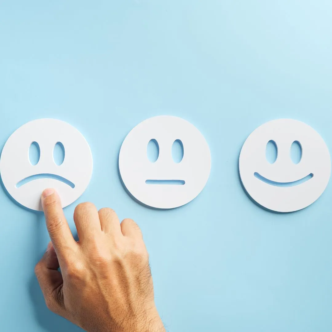 Hand selecting a sad face icon among neutral and happy options, representing customer dissatisfaction