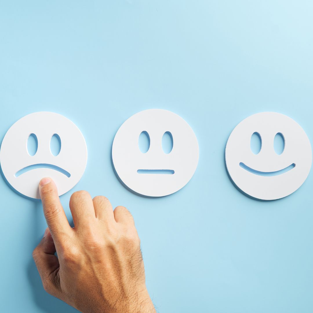 Hand selecting a sad face icon among neutral and happy options, representing customer dissatisfaction