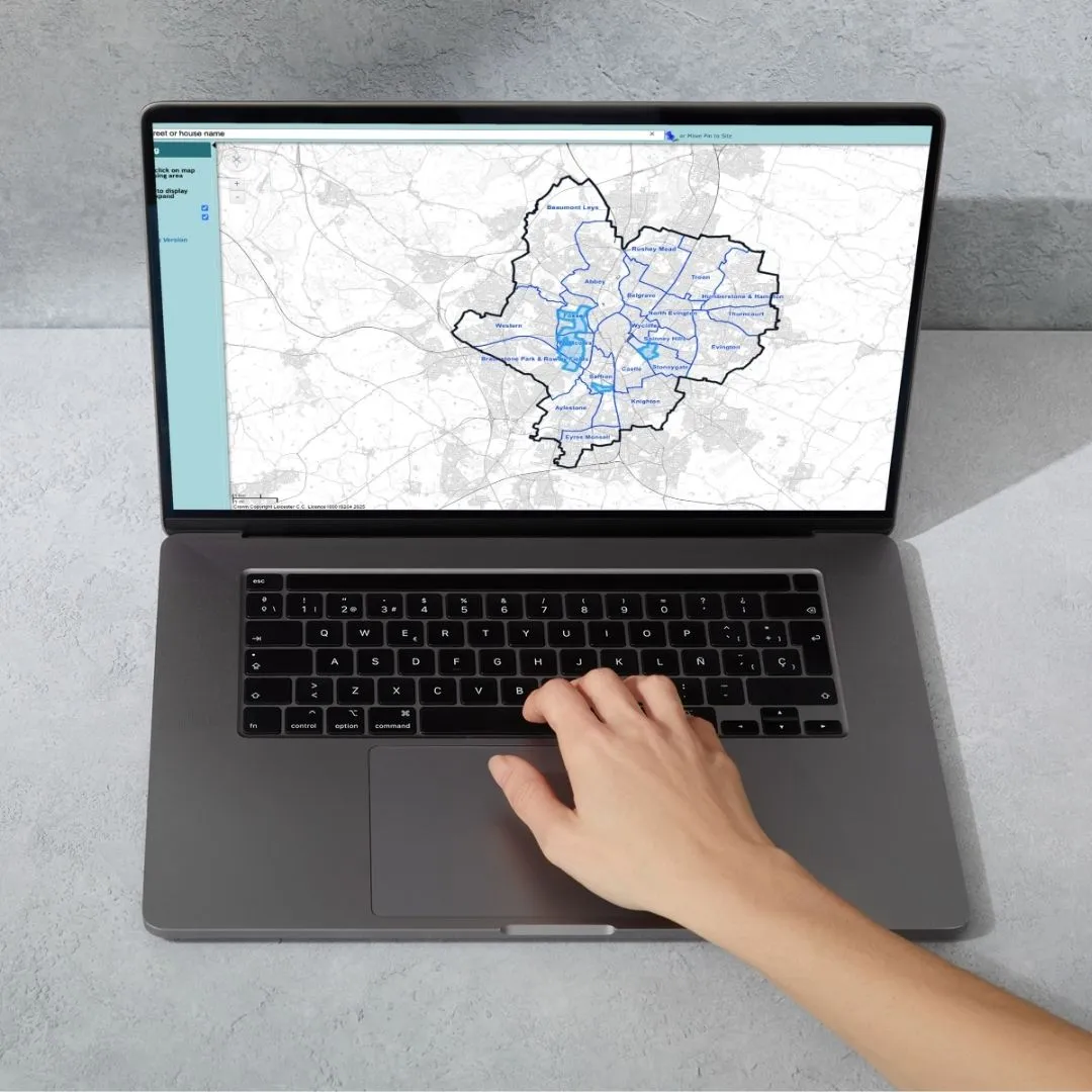 Laptop displaying a map interface with a geographic area outlined in black and shaded in blue, showing various neighborhood names and streets