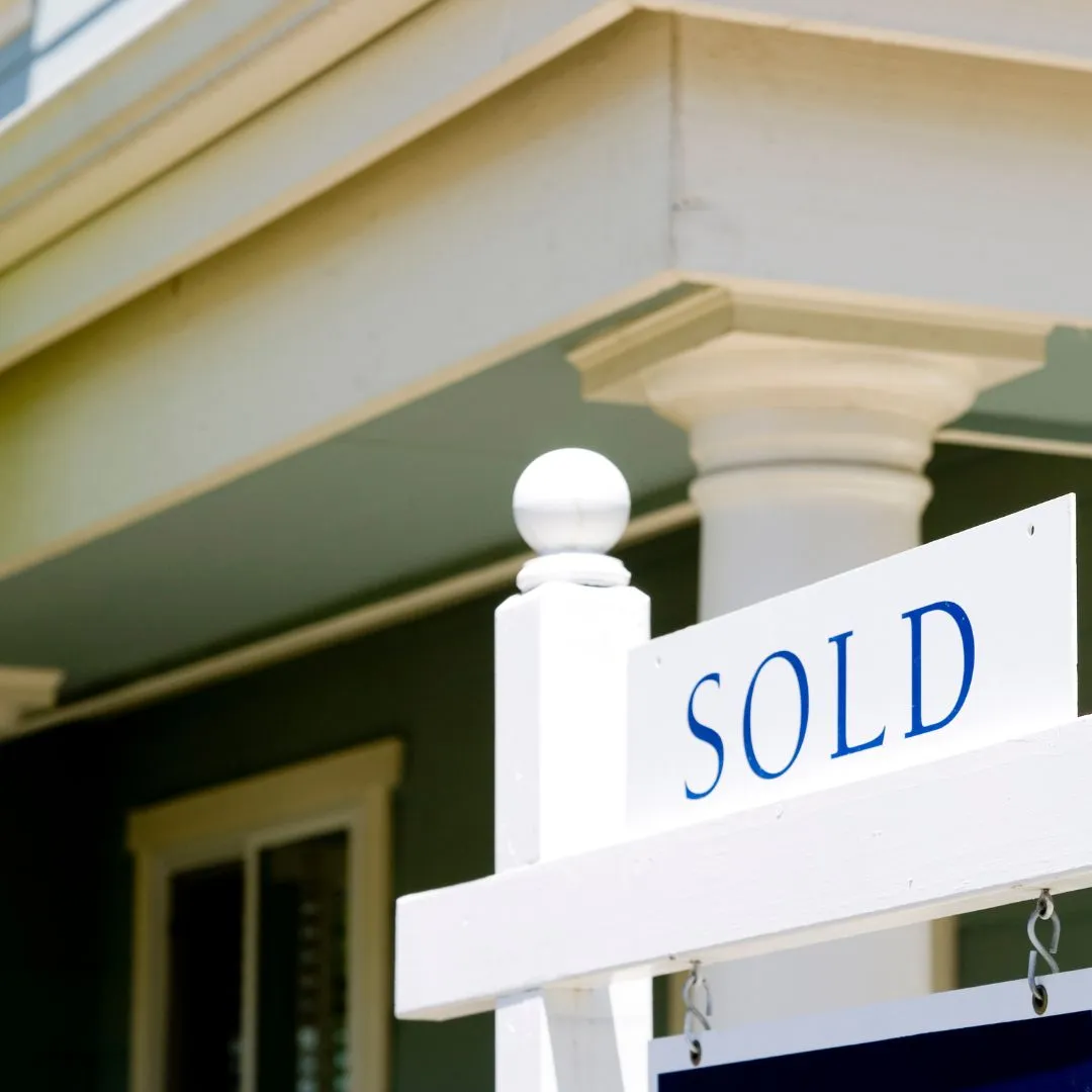 White "SOLD" sign with blue text mounted on a property entrance with green and cream architectural details