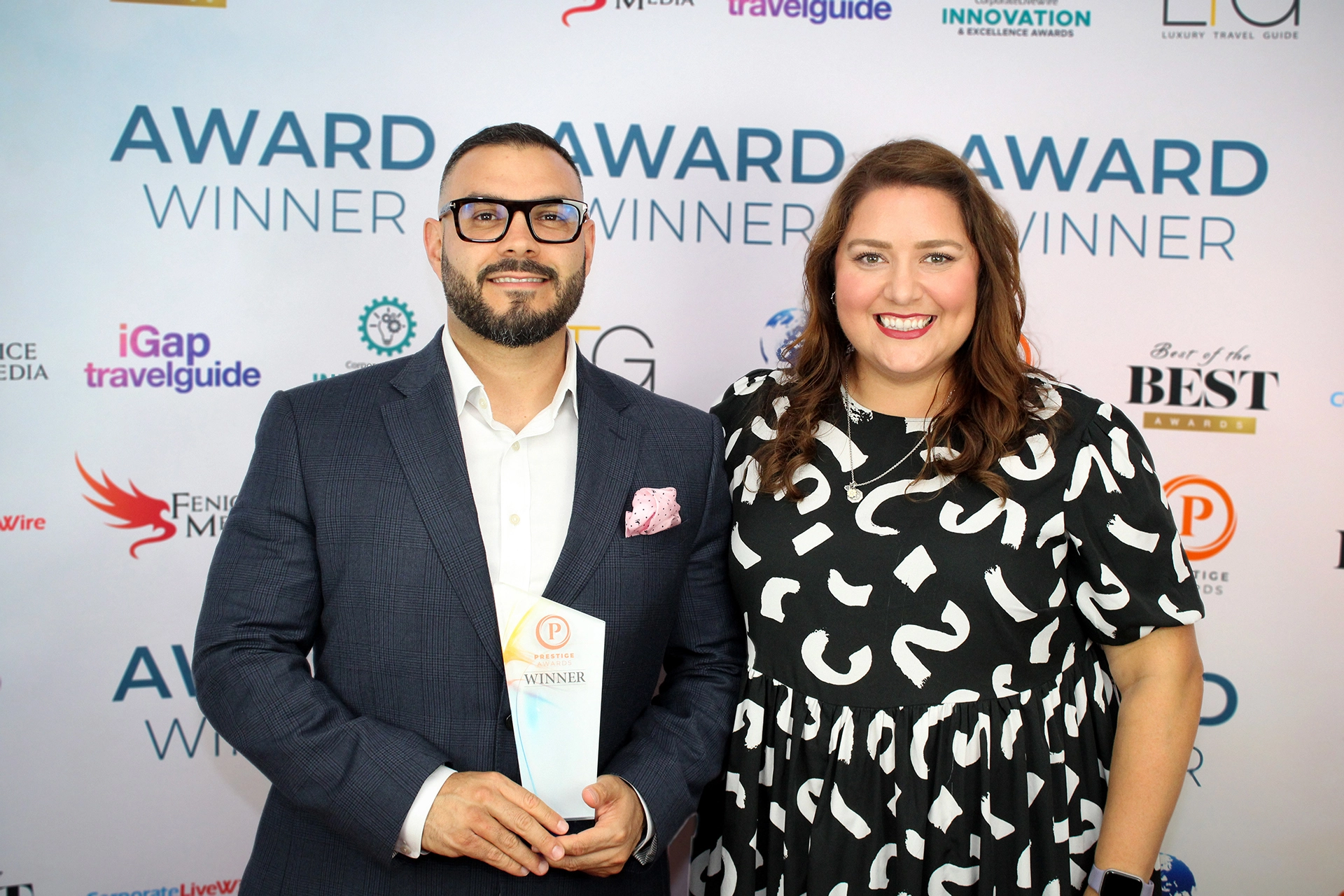 Two people standing in front of an awards backdrop holding a winner award