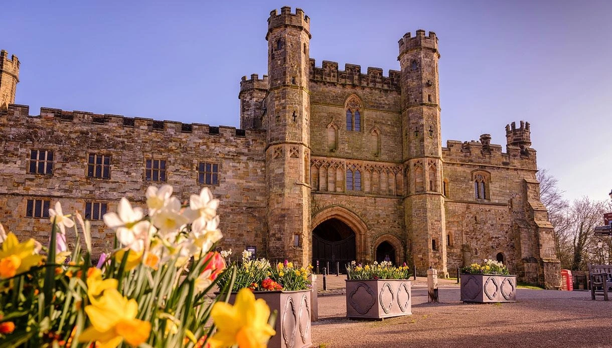 Stone castle with crenellated towers and arched entrance, spring flowers in foreground