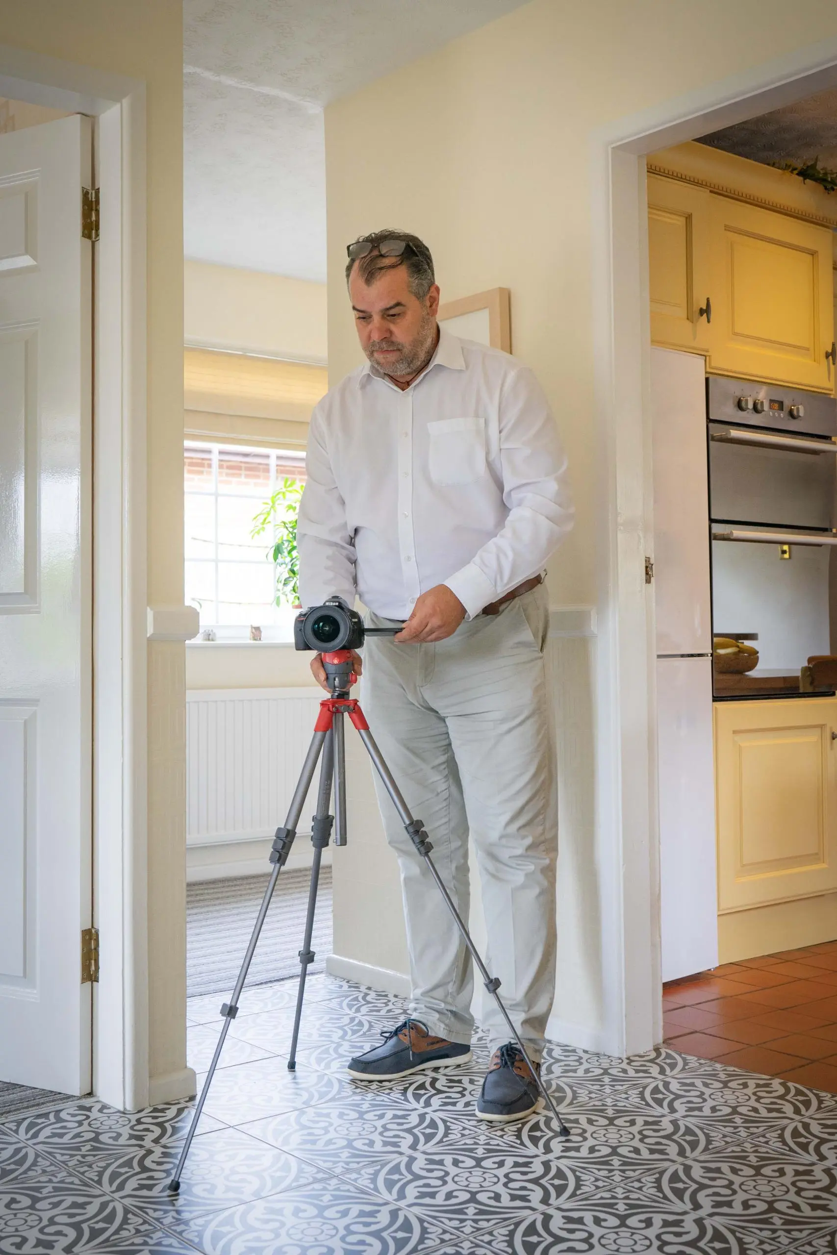 Man with thermal imaging camera on tripod in kitchen with cream walls and yellow cupboards