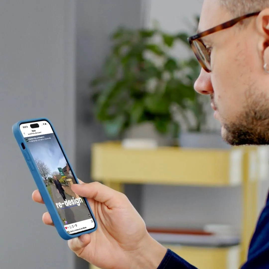 Person wearing glasses holding a blue phone displaying a property listing with "re-design" text visible on screen